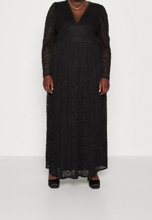Black lace long-sleeve maxi dress with V-neckline, fitted waist, and floral patterns, worn with black square-toe heels and a silver chain necklace.