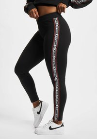 Sorte leggings med en tettsittende design, med røde og hvite logo-trykte sidestriper. Kombinert med hvite Nike joggesko.