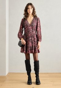 Floral patterned, deep pink dress with a V-neck, long sleeves, and a flared skirt. Paired with black knee-high boots and a small black bag.
