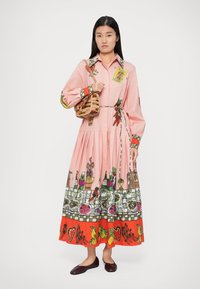 Rochie roz cu mânecă lungă, având partea inferioară cu un model ce ilustrează ustensile de bucătărie și alimente. Dispune de o curea și accente colorate pe guler și manșete.