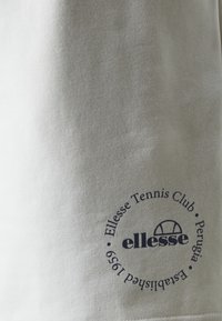 Tejido gris claro con el logo en relieve "Ellesse Tennis Club Perugia" en azul oscuro, diseño circular con el año "1955" indicado. Textura suave.