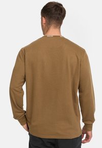 Brun långärmad skjorta med texturerad yta, med rund halsringning och logodetalj på baksidan. Enkel design, avslappnad passform.