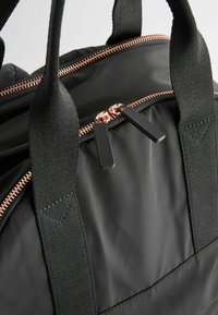 Svart nylon duffelväska med dragkedja i roséguld, svarta detaljer och texturerade svarta remmar, samt platta, rektangulära dragkedja drar.