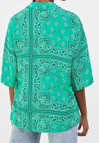 Green paisley-patterned shirt with short sleeves, featuring a relaxed fit and contrasting black accents. Fabric appears smooth and lightweight.