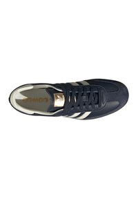 Sneaker Adidas Samba nera con strisce bianche, lacci neri e logo dorato sulla linguetta, vista dall'alto su sfondo bianco.