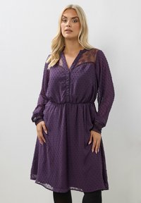 Vestido morado con mangas largas, cierre de botones en la parte delantera, cintura elástica, tejido texturizado, yugo de encaje transparente y patrón de puntos en toda la prenda.
