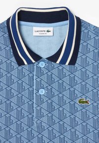 Modrá vzorovaná polo košile s námořnickým límečkem a pruhy, s světle modrými knoflíky a zeleným krokodýlem Lacoste na hrudi.