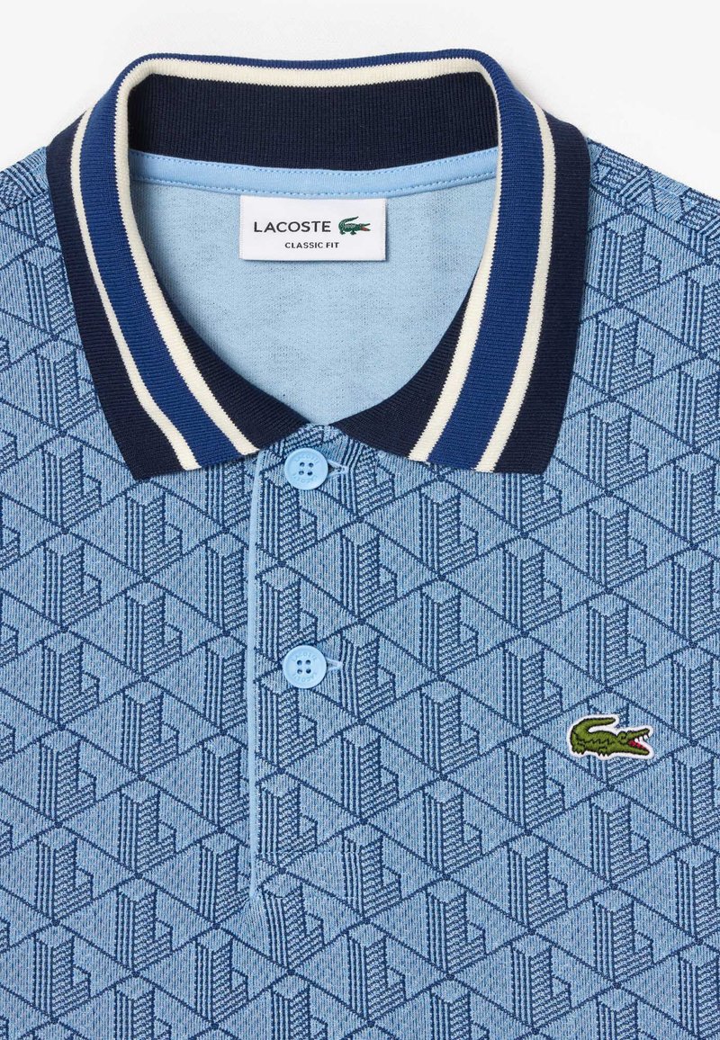 Polo bleu à motifs avec col et rayures bleu marine, doté de boutons bleu clair et d'un logo crocodile Lacoste vert sur la poitrine.