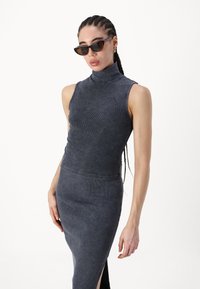 Top cinzento canelado sem mangas com gola alta, combinado com uma saia ajustada a condizer com uma fenda lateral, exibindo um material suave e texturizado.