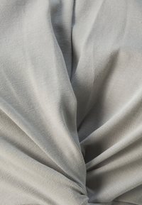 Grått stoff med en glatt tekstur, med et vridd design og subtil ribbing. Foldene skaper dybde og dimensjon i materialet.