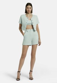 Lichtblauw, textuurgetailleerd driedelig kostuum bestaande uit een cropped jasje, een aansluitend topje en hoge shorts. Bevat knoopaccenten.