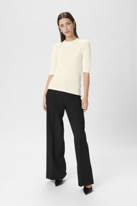 Crepe ribstrikket sweater med korte ærmer parret med sorte vide bukser og spidse sorte hæle. Minimalistisk design og glatte teksturer.
