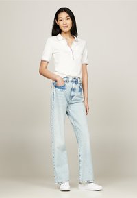 Camisa polo blanca de manga corta con cuello de cremallera, combinada con unos vaqueros de pierna ancha de color azul claro. El conjunto se completa con zapatillas blancas.