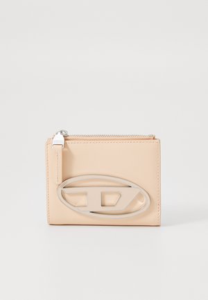 Portefeuille en cuir couleur pêche avec un logo oval en argent. Possède une fermeture à glissière et une texture lisse. Forme rectangulaire compacte.