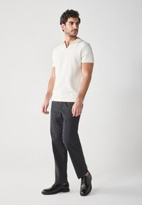 Short-sleeved, ribbed knit polo in off-white, paired with tapered dark trousers and black lace-up shoes, emphasizing a clean, modern silhouette.