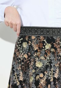 Jupe à motif floral avec une base noire, ornée de broderies dorées, argentées et cuivrées. La ceinture est dotée d'une bande noire texturée avec un motif.