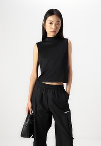 Μαύρο αμάνικο cropped τοπ με ψηλή λαιμόκοψη, συνδυασμένο με χαλαρές μαύρες παντελόνες με ελαστική μέση και πλευρικές τσέπες.