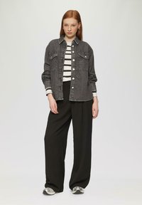 Zwarte denimjas met zilveren knopen, gecombineerd met een zwarte wijde broek en een gestreept shirt met lange mouwen. Zilveren sneakers maken de look af.