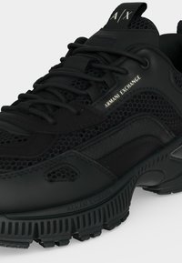 Baskets noires Armani Exchange avec panneaux en mesh texturé et cuir, semelle épaisse à rainures, et détails de marque sur le côté et la languette.