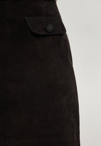 Gonna nera in suede con tasca a pattina dotata di un bottone circolare, superficie testurizzata e cuciture pulite vicino all'orlo.