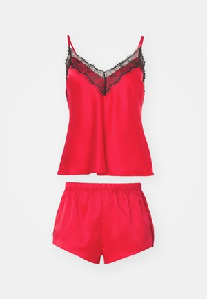 Red satin pajama set featuring a camisole with black lace trim and matching shorts with an elastic waistband. Smooth texture, casual design.