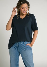 T-shirt blu navy con scollo a V e maniche corte, realizzato in tessuto morbido, abbinato a jeans in denim chiaro e morbidi, e a un orologio beige al polso.