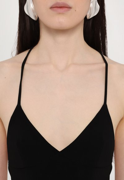 Schwarzes Top mit Spaghettiträgern und V-Ausschnitt. Der Stoff ist glatt und hat einen minimalistischen Stil. Große silberne Ohrringe sind sichtbar.