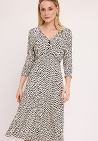 Czarna i biała sukienka w wzory z dekoltem w serek, rękawami o długości trzech ćwierć i rozkloszowanym krojem. Posiada detal w postaci guzika z przodu.