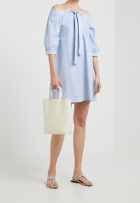 Světle modré šaty s odkrytými rameny a bílými pruhy, se zavazováním u výstřihu a volnými rukávy. Kombinované s krémovou kabelkou a černými žabkami.