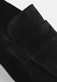 Schwarze Wildlederloafer mit gesticktem Rand, einem flachen Riemen über dem Blatt und einer strukturierten Oberfläche für zusätzlichen Detailreichtum.