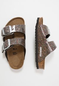 Birkenstock szandál csillogó fekete szintetikus pántokkal, két állítható ezüst csattal, parafa talppal és texturált gumitalppal.