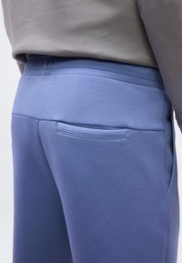 Κοντινό πλάνο ατόμου που φοράει μπλε παντελόνι με πίσω τσέπη τύπου welt και γκρι πουκάμισο μπα tucked-in.