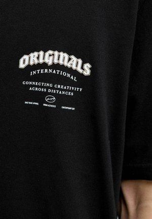 Black cotton t-shirt featuring a large white and cream graphic print with text: "ORIGINALS INTERNATIONAL CONNECTING CREATIVITY ACROSS DISTANCES."