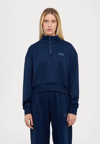 Navy zippered sweatshirt with cropped design, long sleeves, and soft texture. Features "7 Days Active" logo in light blue.