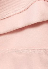 Vaaleanpunainen huppari, jossa on päällä sileä fleecekerros ja ribbatekstuuri helman kohdalla, sekä näkyvät ompeluyksityiskohdat.