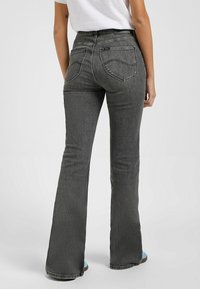 Jean noir évasé avec une taille haute, doté de poches arrière et de détails de couture visibles, présenté de dos. Texture de denim lisse.