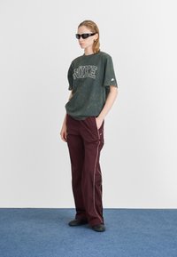 Zaļas marmora pārspīlētas T-kreklu ar "NIKE" uzrakstu, saskaņojot ar vīna sarkanām platām biksēm ar baltām sānu svītrām un melnām kurpēm.