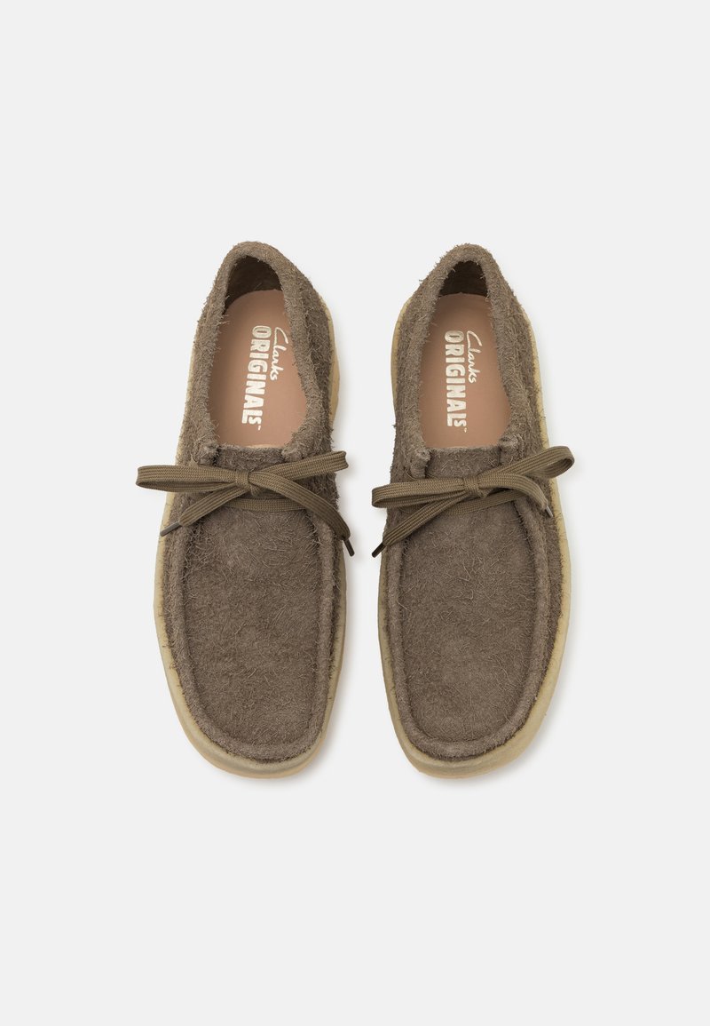 Chaussures en suède marron avec une finition texturée, dotées d'un lacet fin à l'avant et d'une semelle en caoutchouc crème. Design doux et arrondi.