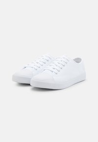 Zapatillas de lona blancas con un diseño de caña baja, puntera redonda, cordones en la parte delantera y suelas de goma con detalles texturizados.