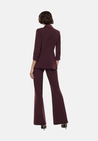 Blazer su misura bordeaux con maniche a tre quarti e pantaloni svasati coordinati. Tessuto liscio, design semplice e silhouette aderente.