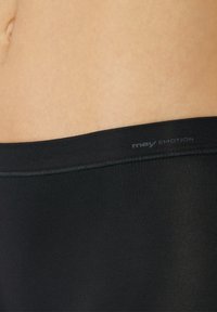 Svarta leggings gjorda av stretchigt tyg med en slät yta, försedda med en midjeresår märkt "mily Emotion" längs det övre kant.