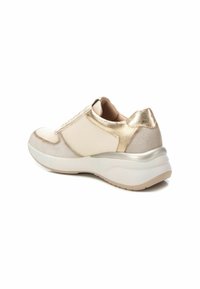 Zapatilla de color claro con una combinación de materiales lisos y texturizados. Presenta acentos metálicos en el talón, una suela acolchada y un diseño de cordones.