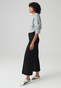 Lichtgrijze, textuurtrui met geribbelde manchetten, gecombineerd met hoge zwarte wijde broek en witte sneakers met zwarte accenten.