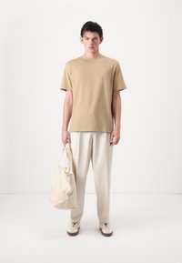 Beige bomulds t-shirt, afslappet pasform, båret med cremede bukser og en matchende tote bag. Sneakers med lys overdel og brune såler.