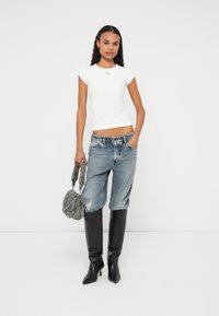 Vit figursydd t-shirt med korta ärmar, slitna ljusblå jeans, svarta knähöga stövletter med klack och en grå texturerad handväska.