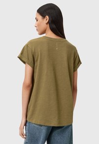 Olivenfarbiges Baumwoll-T-Shirt mit umgeschlagenen kurzen Ärmeln, Rundhalsausschnitt und kleinem Logo hinten am Nacken. Lockere Passform.