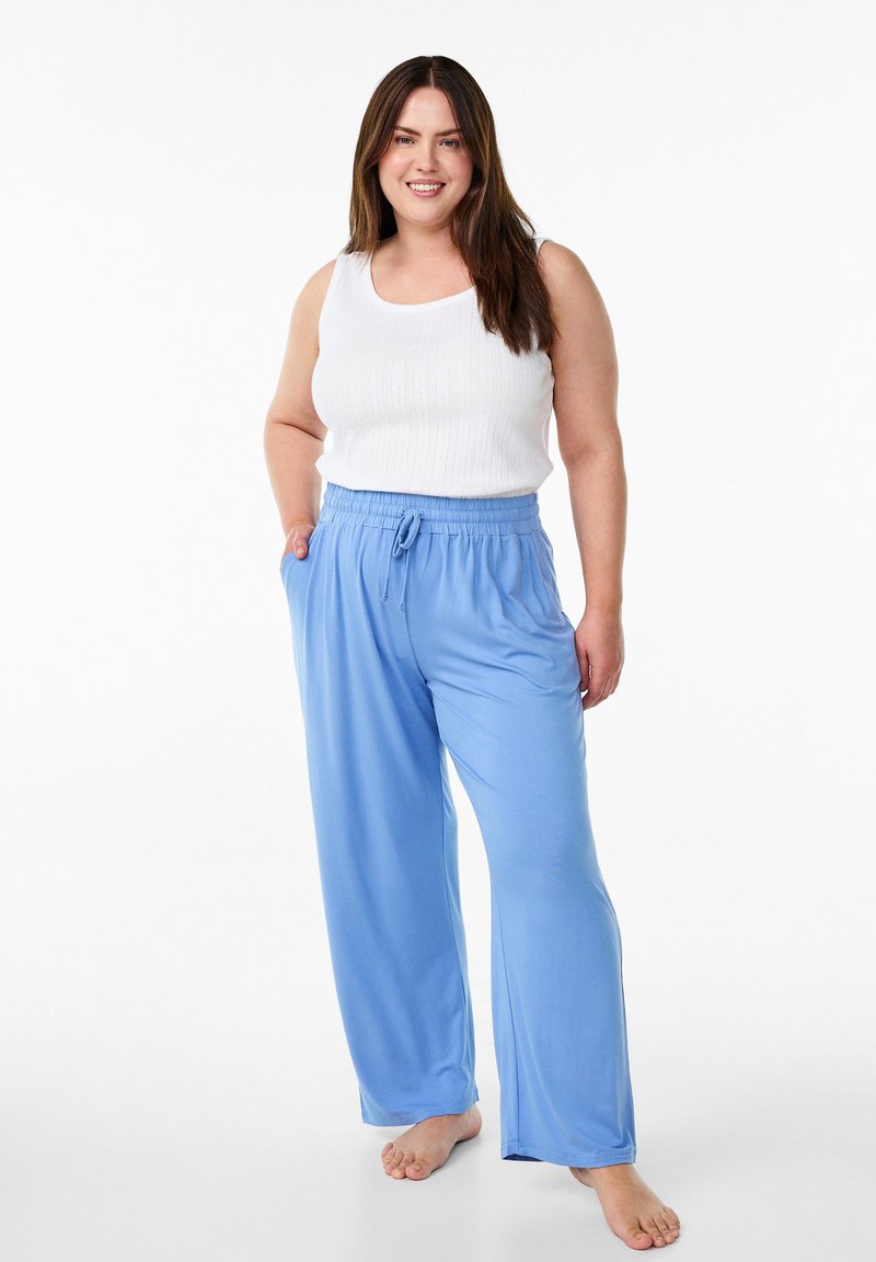 Pantalon large bleu clair avec une taille élastique et un cordon de serrage, associé à un débardeur blanc à côtes. Texture de tissu lisse.
