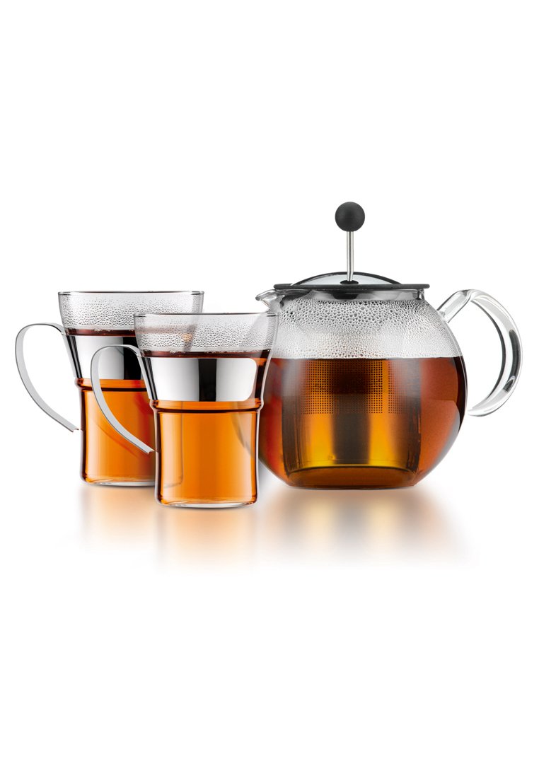 Klarer Glasteekanne mit einem schwarzen Deckel und Griff, daneben zwei passende Gläser mit silbernen Akzenten, gefüllt mit bernsteinfarbigem Getränk.