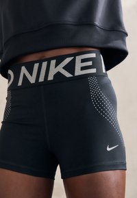 Fekete sportos rövidnadrág rugalmas anyagból, széles elasztikus derékkal, ami a "NIKE" logót viseli, és pöttyös mintázatú díszítéssel az oldalakon.