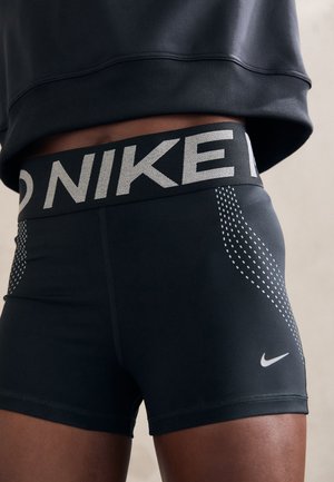 Schwarze Sportshorts aus dehnbarem Material, mit einem breiten elastischen Bund, der das "NIKE"-Logo trägt, und gepunkteten Designelementen an den Seiten.